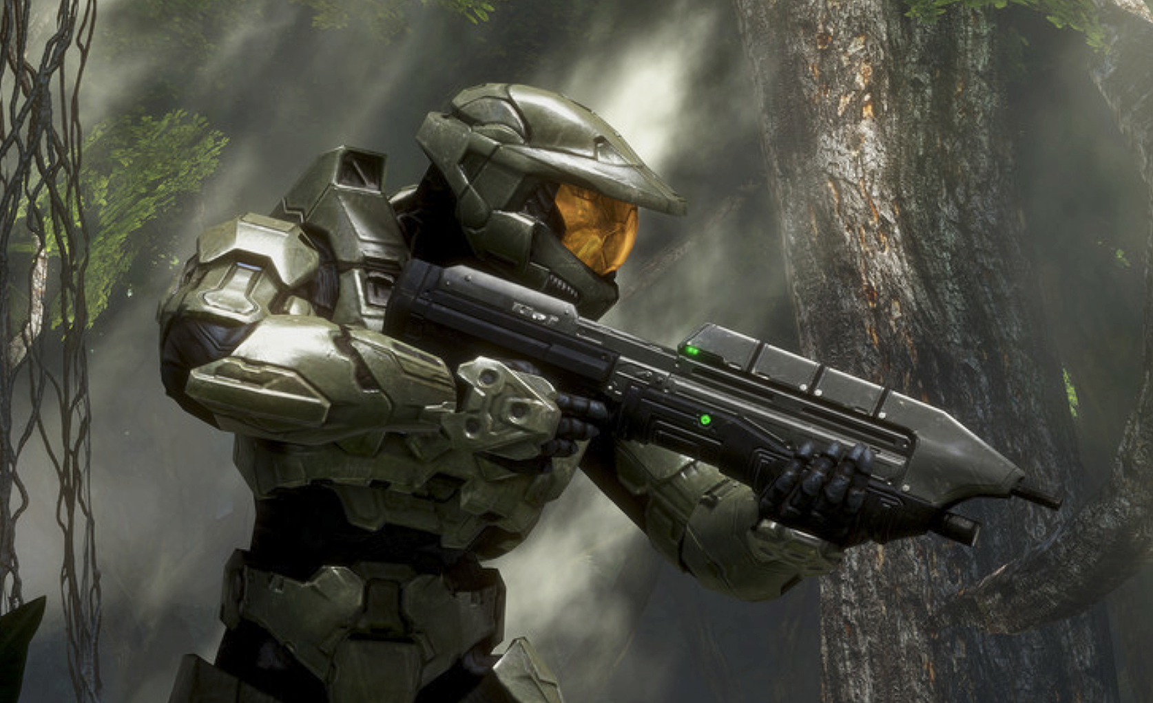 Master Chief i grön rustning med gulbrun visir siktar med ett automatgevär i en solbelyst djungel med tjocka trädstammar och hängande lianer.