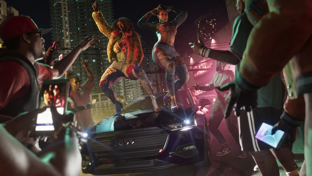 Två kvinnor dansar på motorhuven på en mörk bil under en gatufest i Grand Theft Auto VI, omgivna av jublande folk som filmar med mobiler.