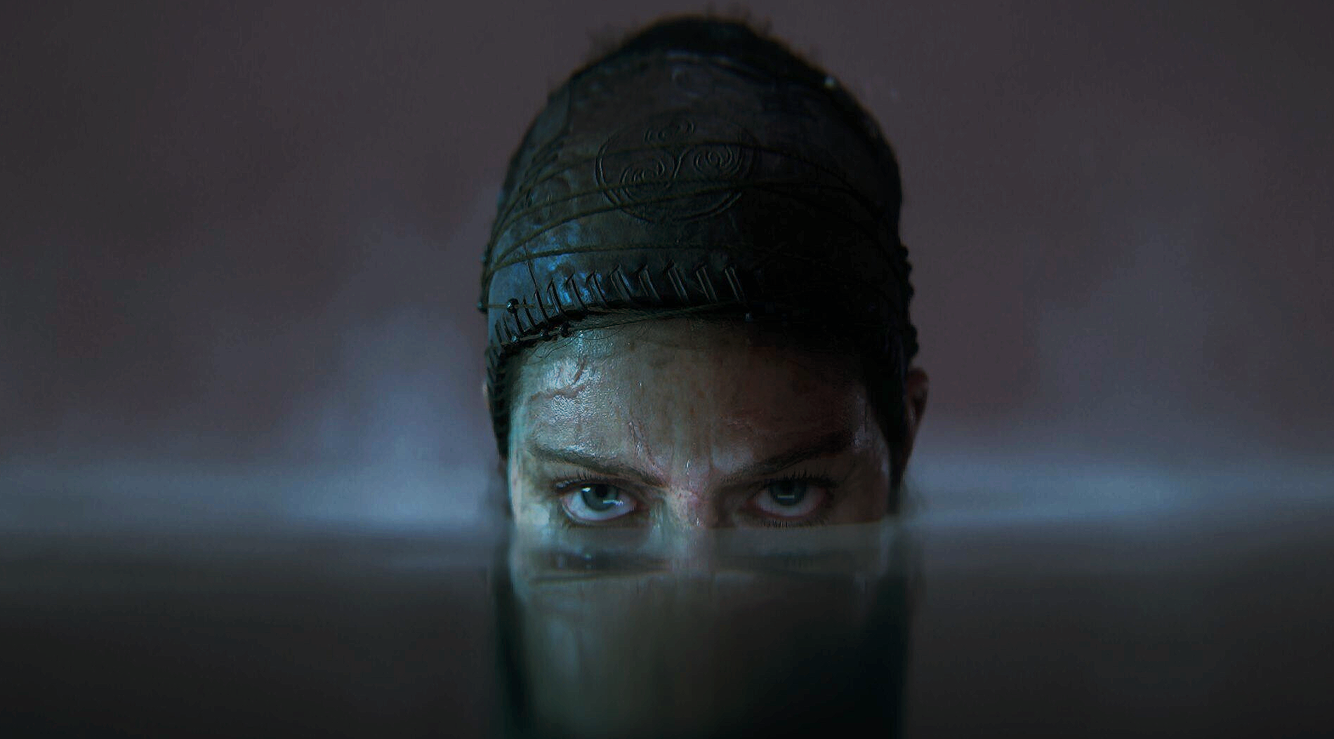 Senua i Senua's Saga: Hellblade II stirrar med blå ögon rakt fram med ansiktet halvt under vattenytan, med mörkt tygband runt huvudet.