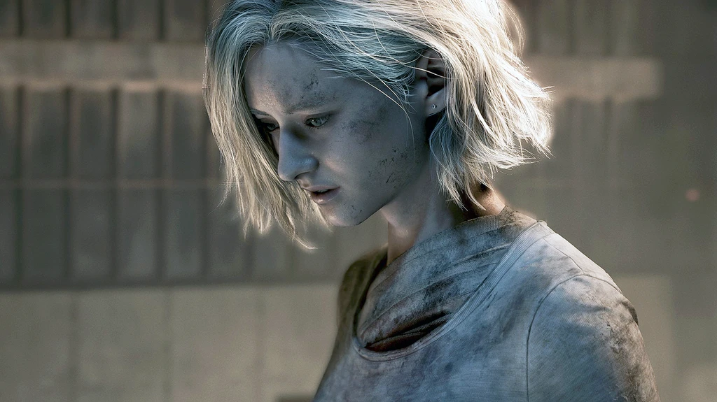 Närbild på en smutsig, blond kvinnlig karaktär med kort hår som blickar nedåt med allvarlig min, i en dunkel betongmiljö i Resident Evil: Requiem.