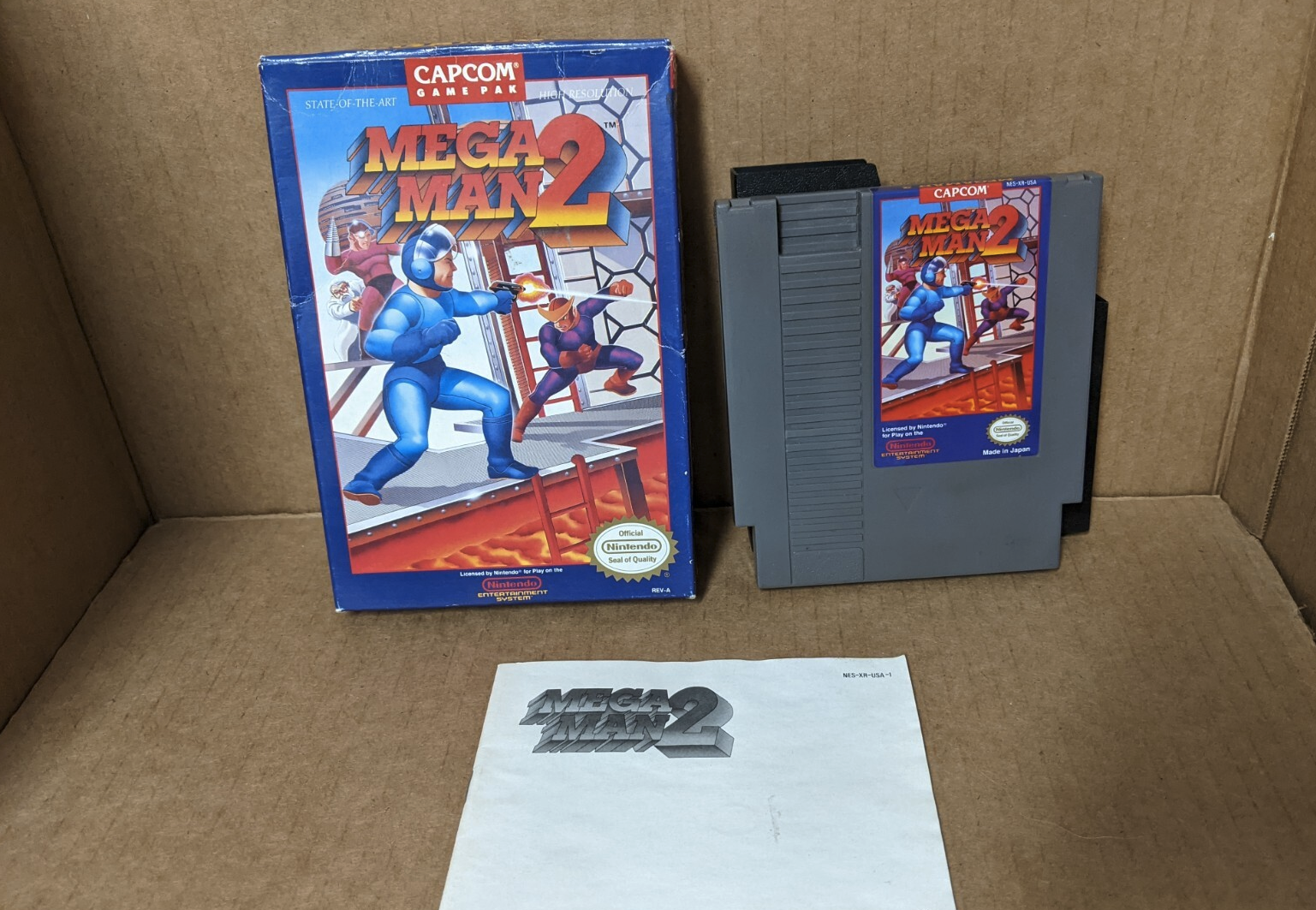 Mega Man 2 till NES: kartongen med Mega Man i blå rustning, det grå spelkortet och manualen ligger i en kartong.