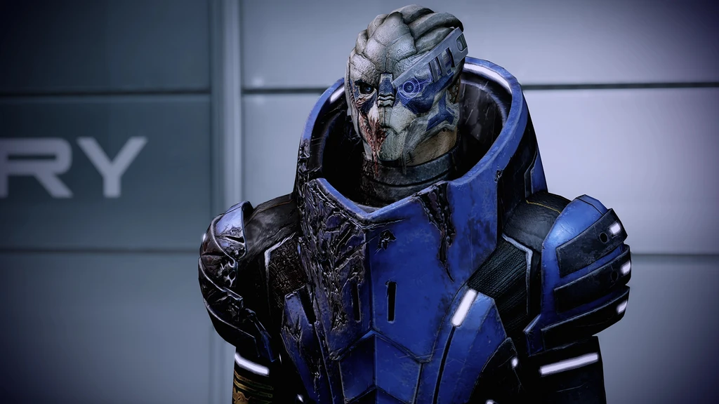 En turian i blå, skadad pansarrustning med visir över ena ögat och ärr i ansiktet står i en metallisk korridor. Scenen är från ett Mass Effect-spel.