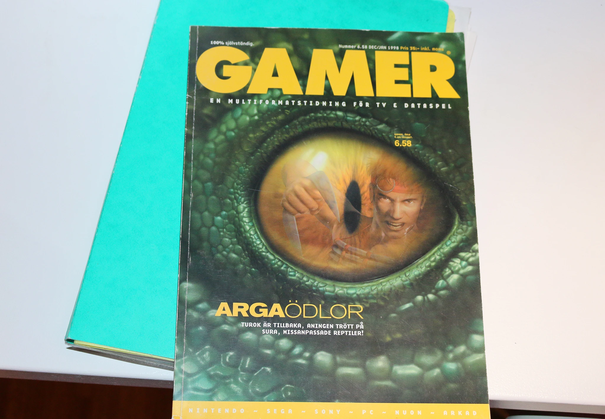 Omslaget till speltidningen Gamer från dec/jan 1998 med ett grönt reptilöga i närbild, där en krigare med pannband syns i pupillen. Rubriken lyder "Arga ödlor".