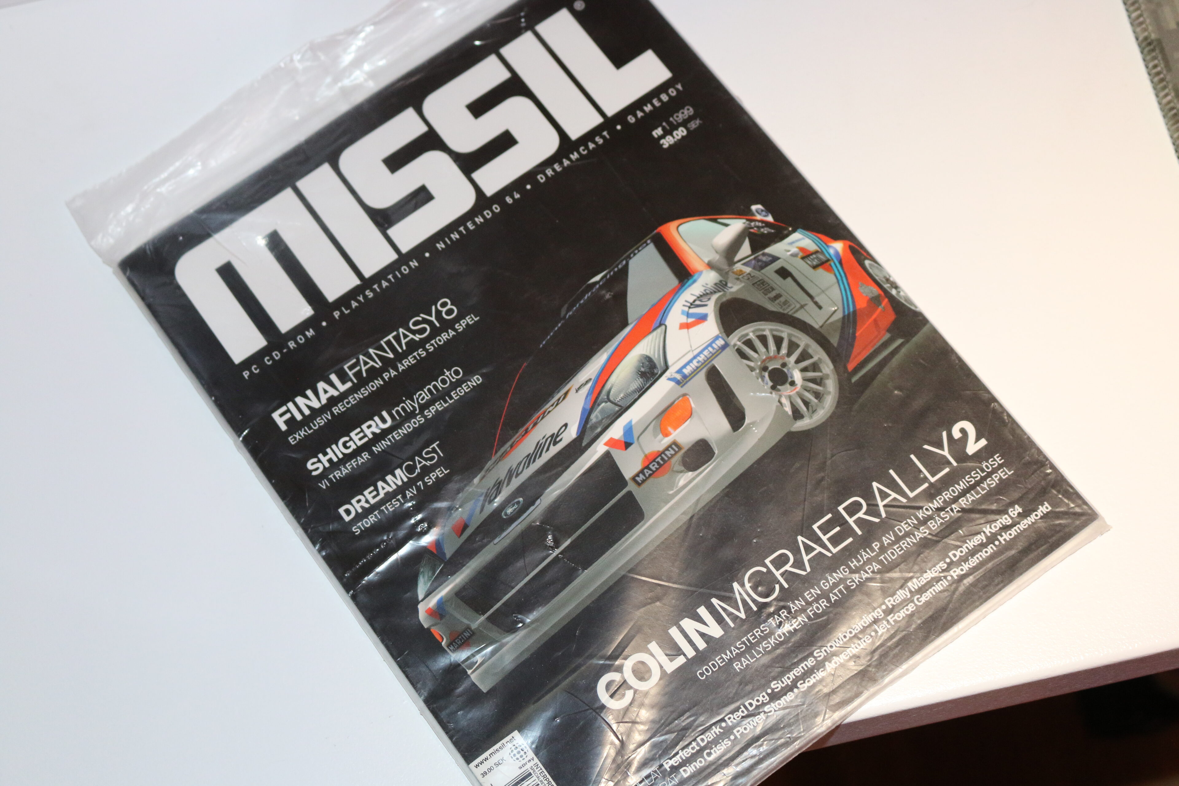 Första numret av speltidningen MISSIL från 1999 i plastficka på ett vitt bord. Omslaget visar en Ford Focus rallybil i Martini-färger från Colin McRae Rally 2.