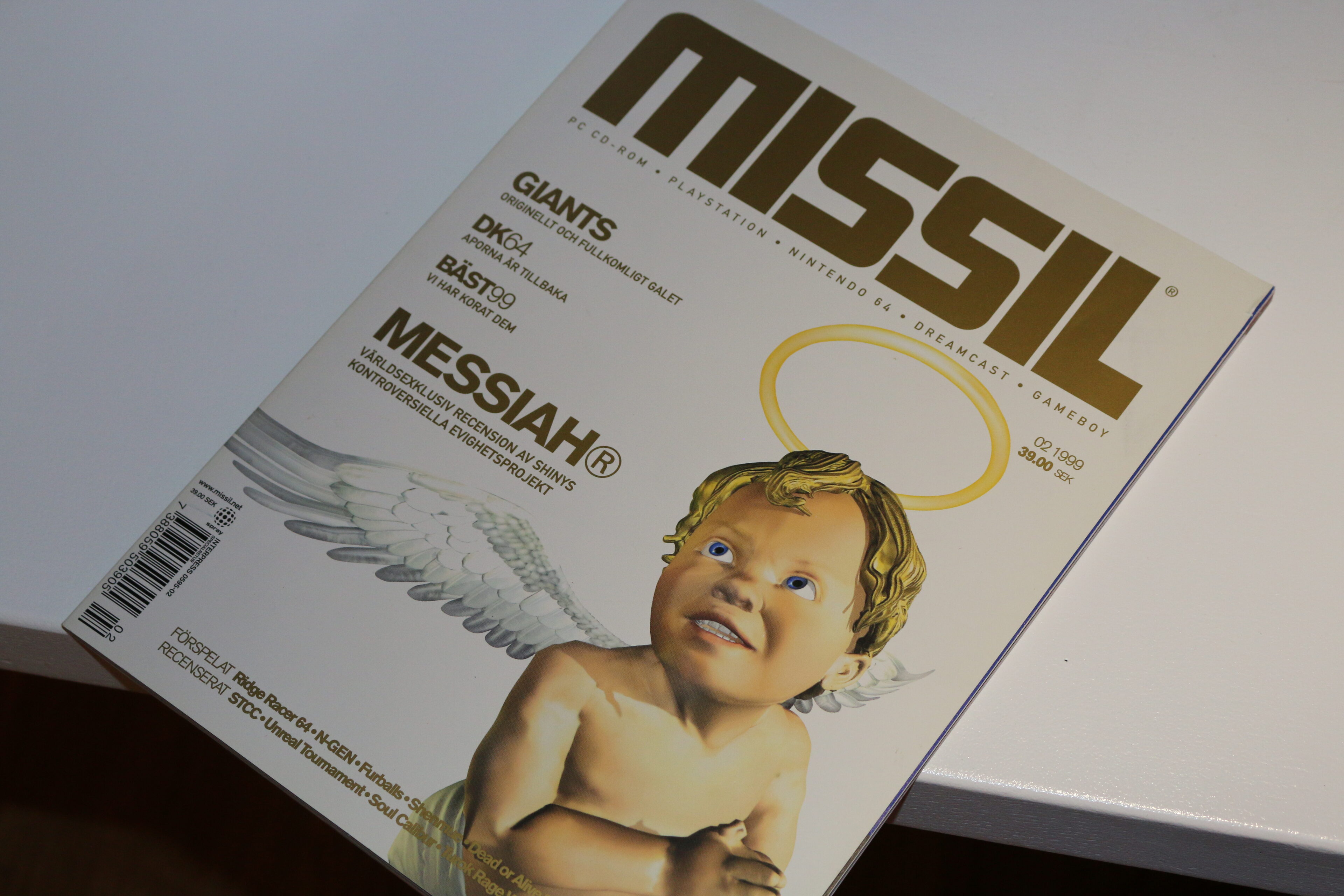 Omslaget till speltidningen MISSIL, nummer 02 1999, med en 3D-renderad ängel med gloria och vingar. Tidningen ligger snett på en vit yta, och omslaget lyfter fram Messiah, Giants och DK64.