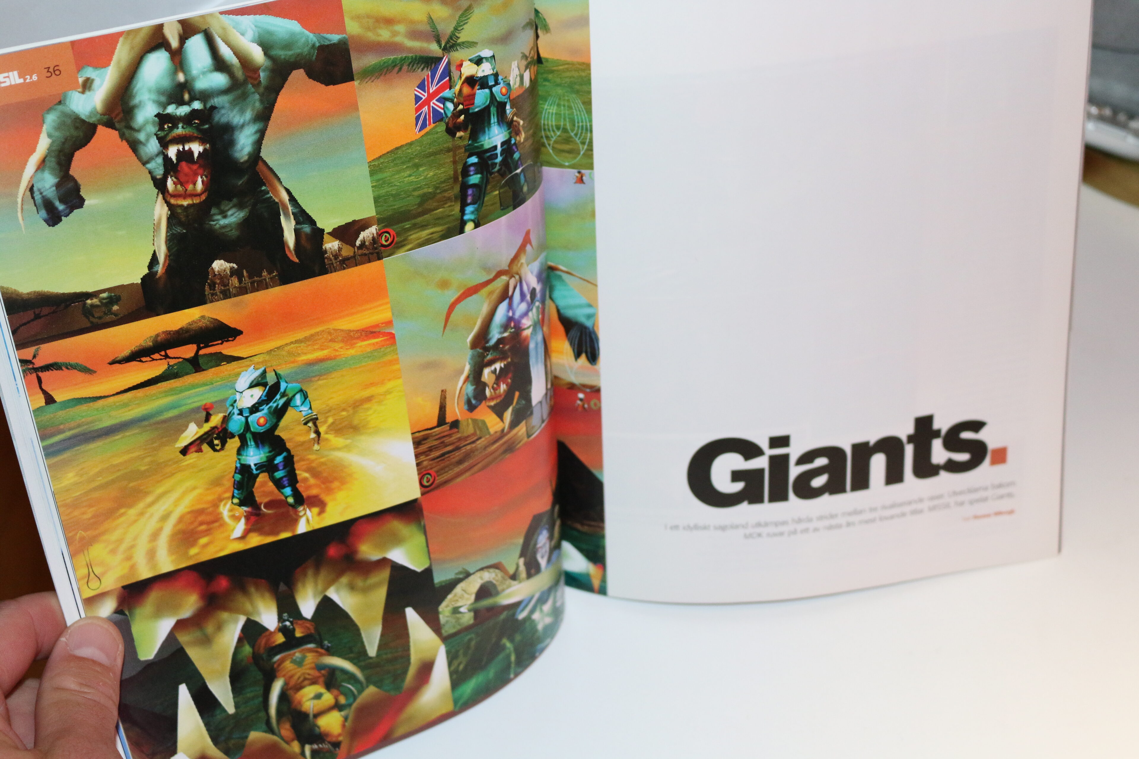 Uppslag i en tidning med spelet Giants: färgstarka skärmdumpar av en jättelik, tandad varelse och en soldat i blå rustning, intill en sida med rubriken Giants.