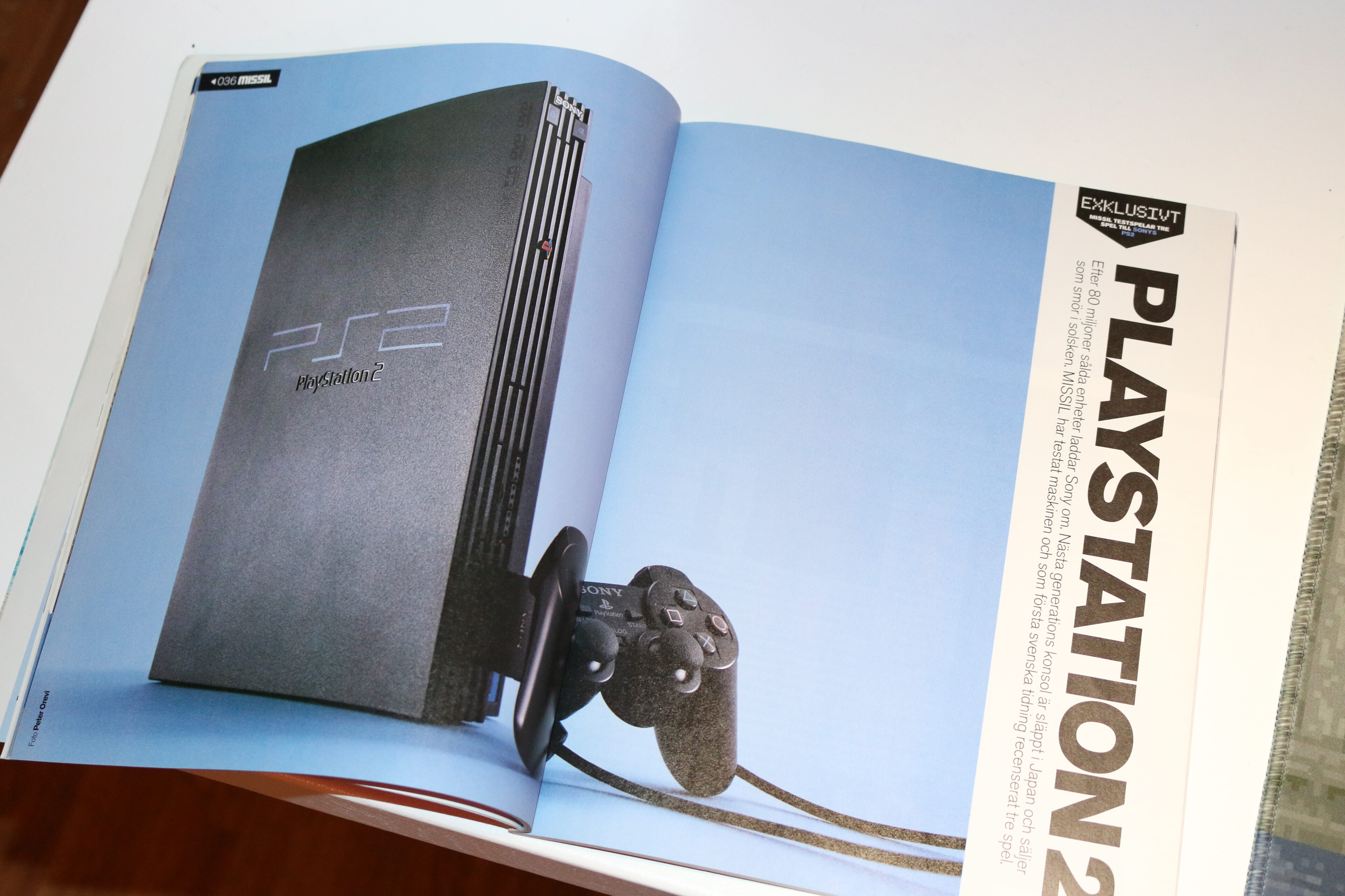 Uppslag i tidningen MISSIL med en svart Playstation 2-konsol stående mot blå bakgrund, med kontrollen lutad mot sidan. Rubriken till höger lyder Playstation 2 och märkt Exklusivt.