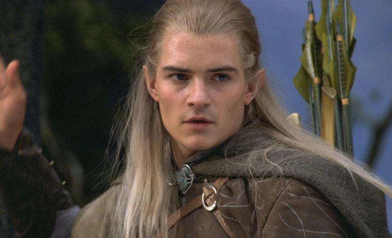 En alv med långt ljust hår, spetsiga öron och grå kappa över brun rustning ttittar allvarligt åt sidan, med pilar på ryggen. Scen ur The Lord of the Rings.
