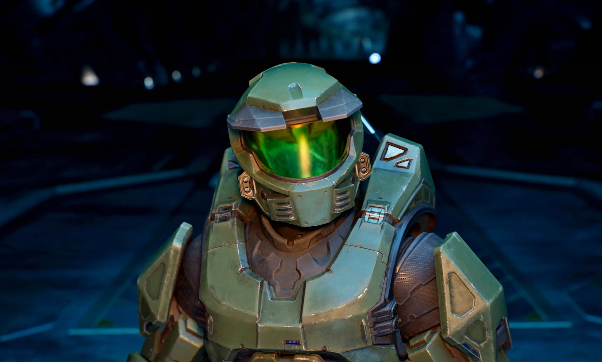 Närbild på Master Chief i grön rustning med grönt, glänsande visir i en mörk, blåtonad rymdmiljö i Halo.