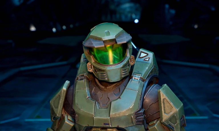 Närbild på Master Chief i grön rustning med grönt, glänsande visir i en mörk, blåtonad rymdmiljö i Halo.
