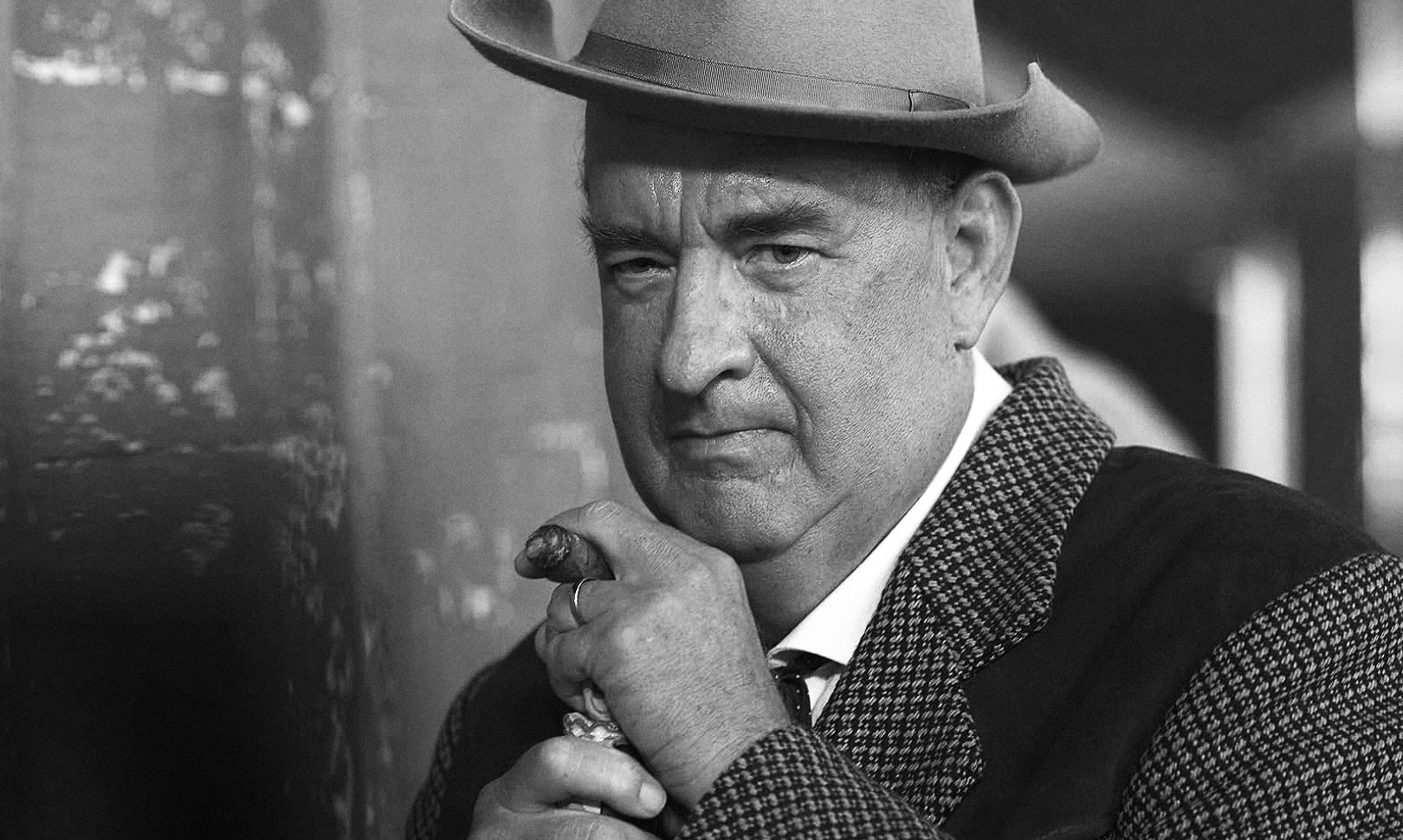 Svartvit närbild av en man i hatt och rutigt kavajställ som med allvarlig min håller en cigarr mot hakan.