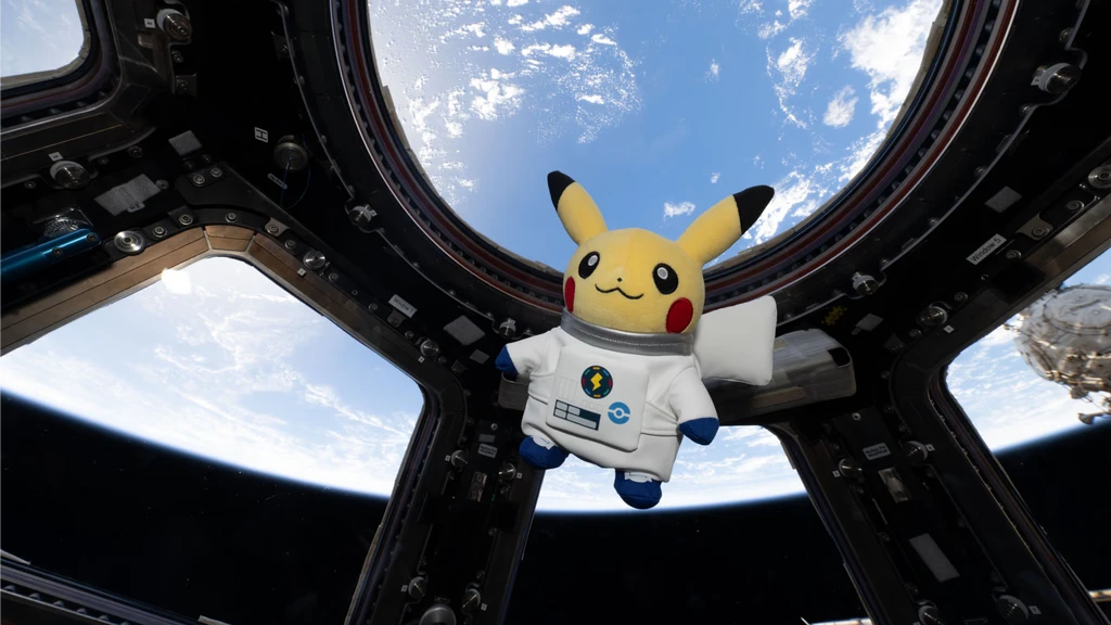 Pikachu-gosedjur i vit astronautdräkt svävar framför de stora fönstren i en rymdstation, med jorden och moln i bakgrunden.
