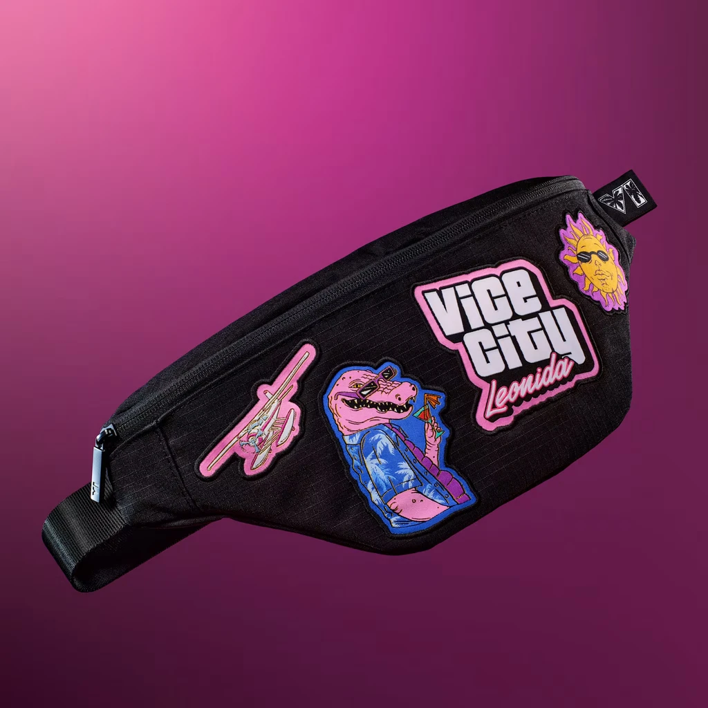 Svart magväska med färgglada lappar: en rosa krokodil i hawaiiskjorta med drink, ett litet flygplan, en solgubbe med solglasögon och en logotyp med texten Vice City Leonida, mot rosa lila bakgrund.