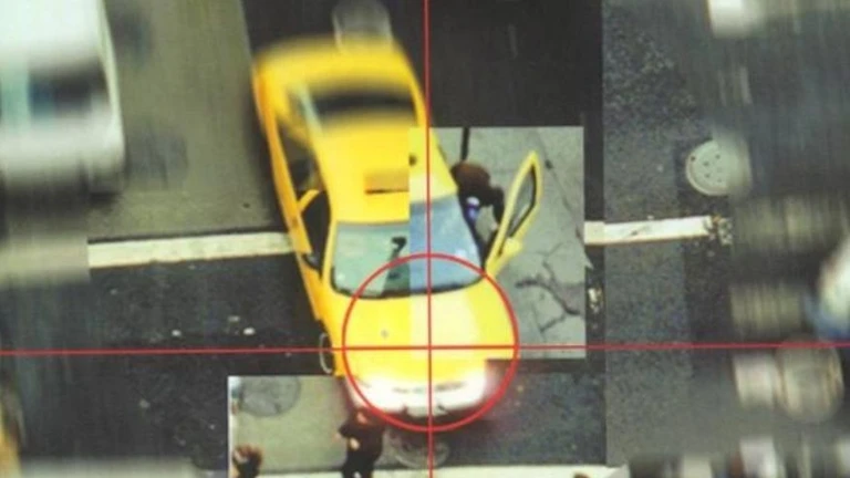 Ovanifrån syns en gul taxi på en gata med en röd sikteskors över framrutan, medan en man står vid den öppna dörren. Grand Theft Auto 2.