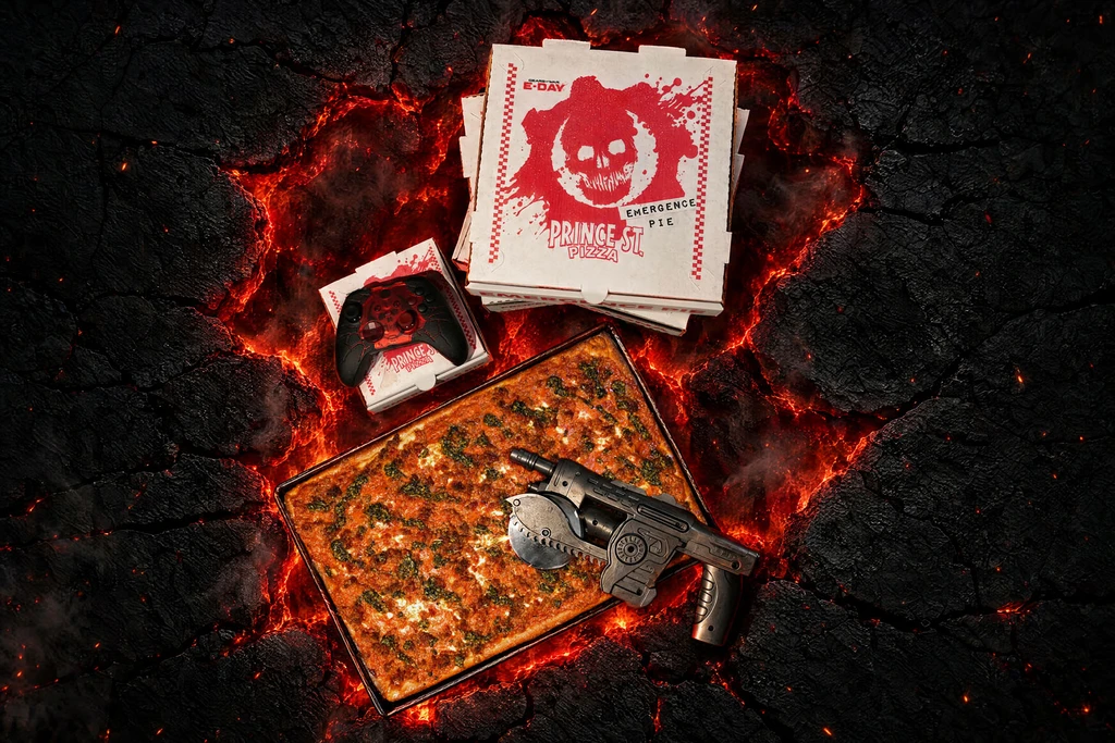 Rektangulär pizza i en plåt på sprucken, glödande lavamark, med pizzakartonger märkta med Gears of War-skallen, en svart Xbox-handkontroll och en pizzaskärare formad som ett Lancer-gevär.