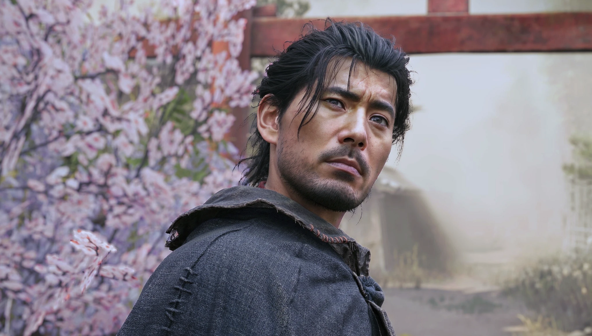 Svartlockig man med skäggstubb och allvarlig blick, klädd i sliten grå mantel, tittar över axeln framför blommande körsbärsträd och en röd torii-port i Onimusha: Way of the Sword.