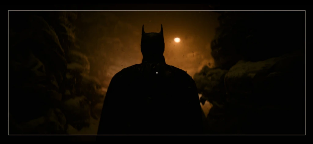 Batman syns som en mörk siluett bakifrån med spetsiga öron, i en trång, snötäckt klippig passage under en glödande orange måne eller lampa.