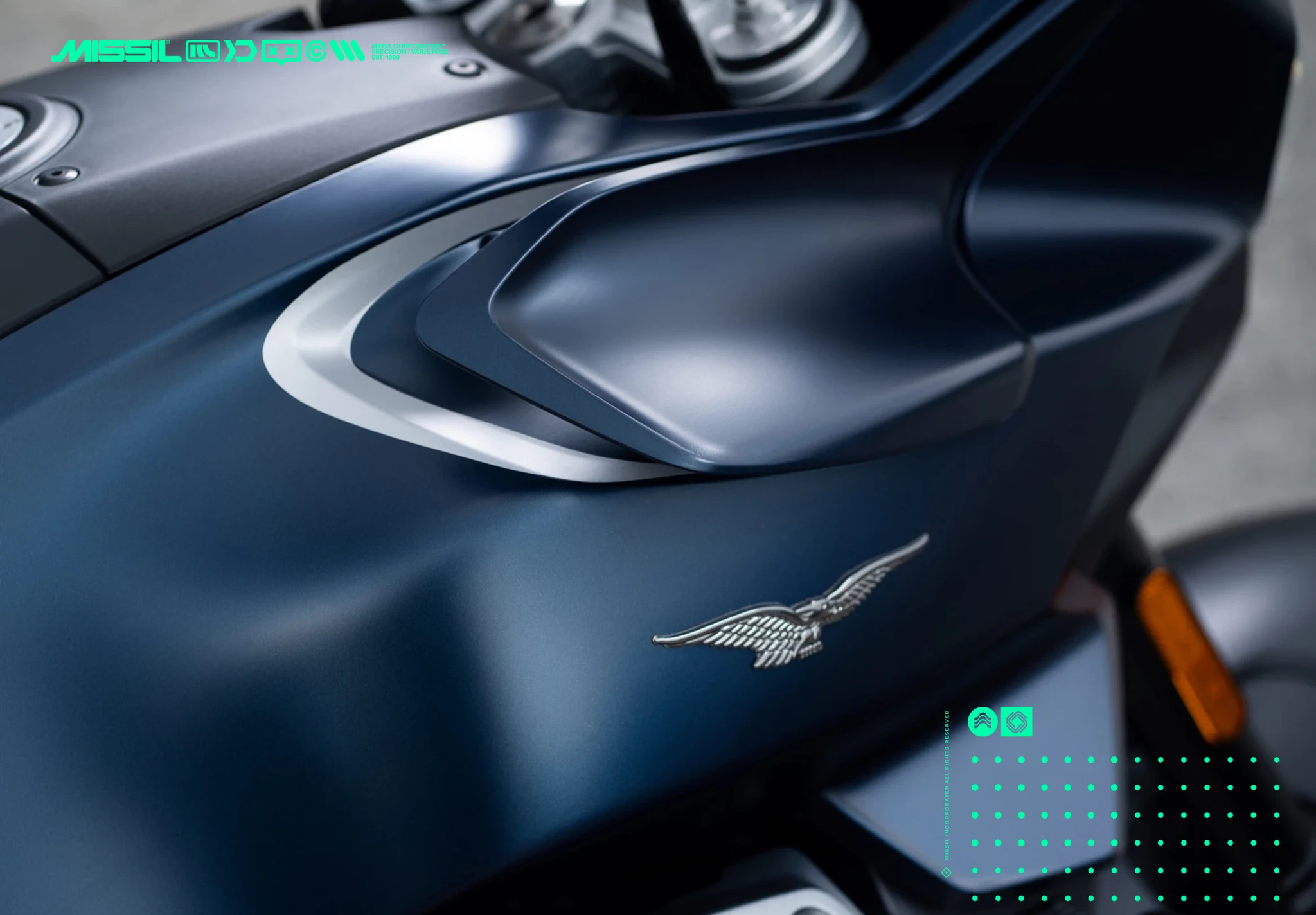 Närbild på tanken och sidopanelen på en matt mörkblå motorcykel med silverfärgad örnlogotyp, som ser ut som Moto Guzzis emblem.