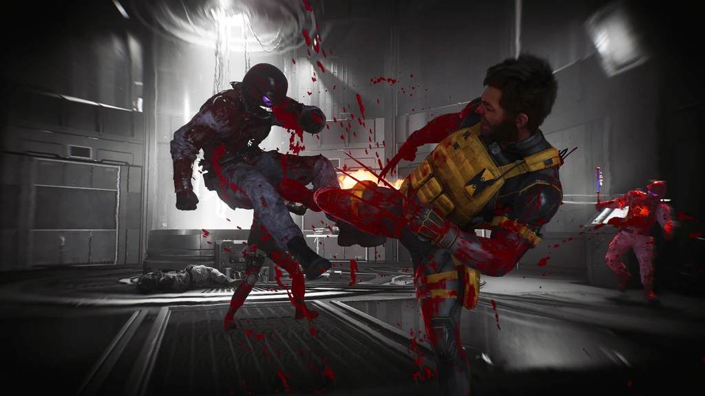Marvel's Wolverine: en man med skäggstubb och gul stridsväst sparkar en pansarklädd fiende i en dunkel, nedsmetad korridor, medan blod stänker och en till fiende närmar sig.