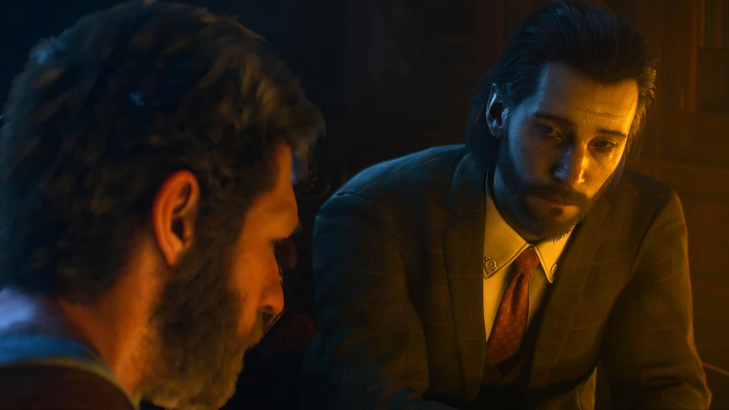 Två skäggiga män sitter nära varandra i ett svagt, varmt upplyst rum i Marvel's Wolverine. Mannen till höger i kavaj och slips tittar allvarligt ner medan den andra syns i profil.