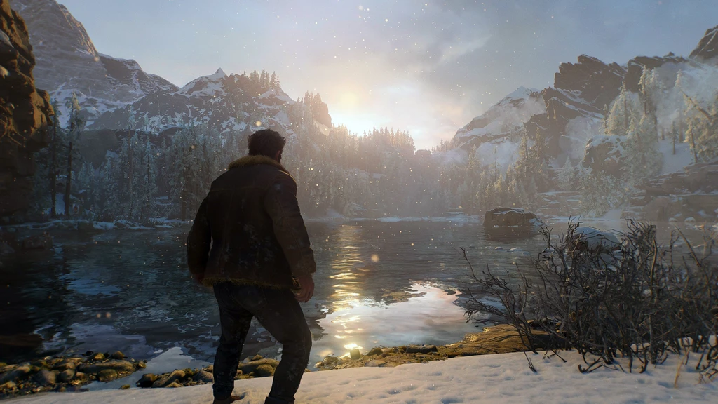 Man i skinnjacka med ryggen mot kameran står vid en snötäckt sjöstrand och blickar mot solen som går upp bakom bergen i Marvel's Wolverine.