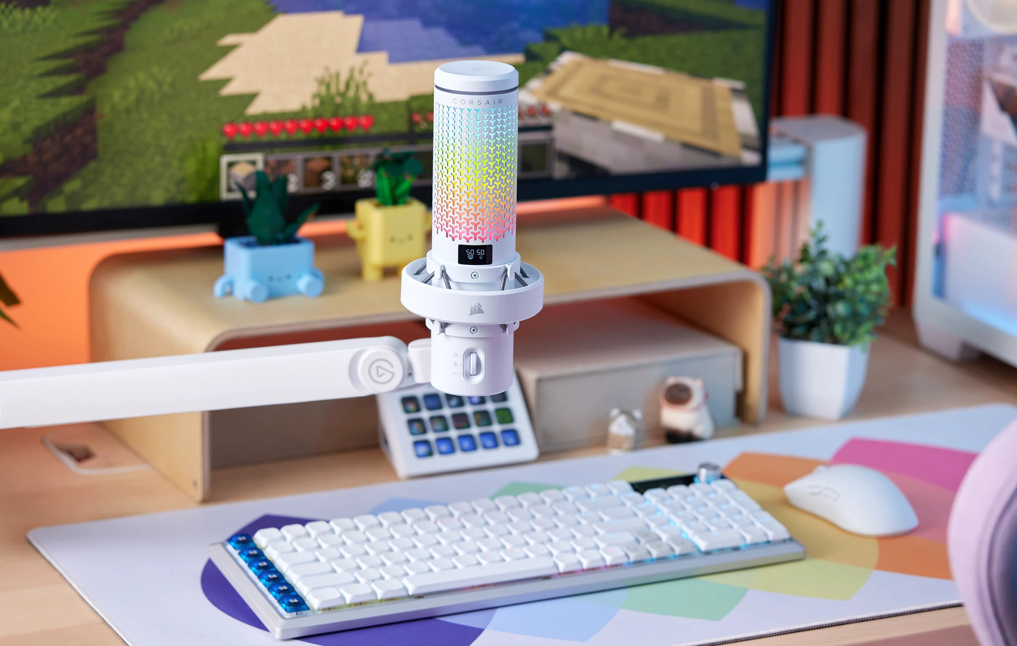 Vit Corsair-mikrofon med färgglad RGB-belysning på en mikrofonarm, på ett skrivbord med vitt tangentbord, mus, musmatta och en bildskärm som visar Minecraft.