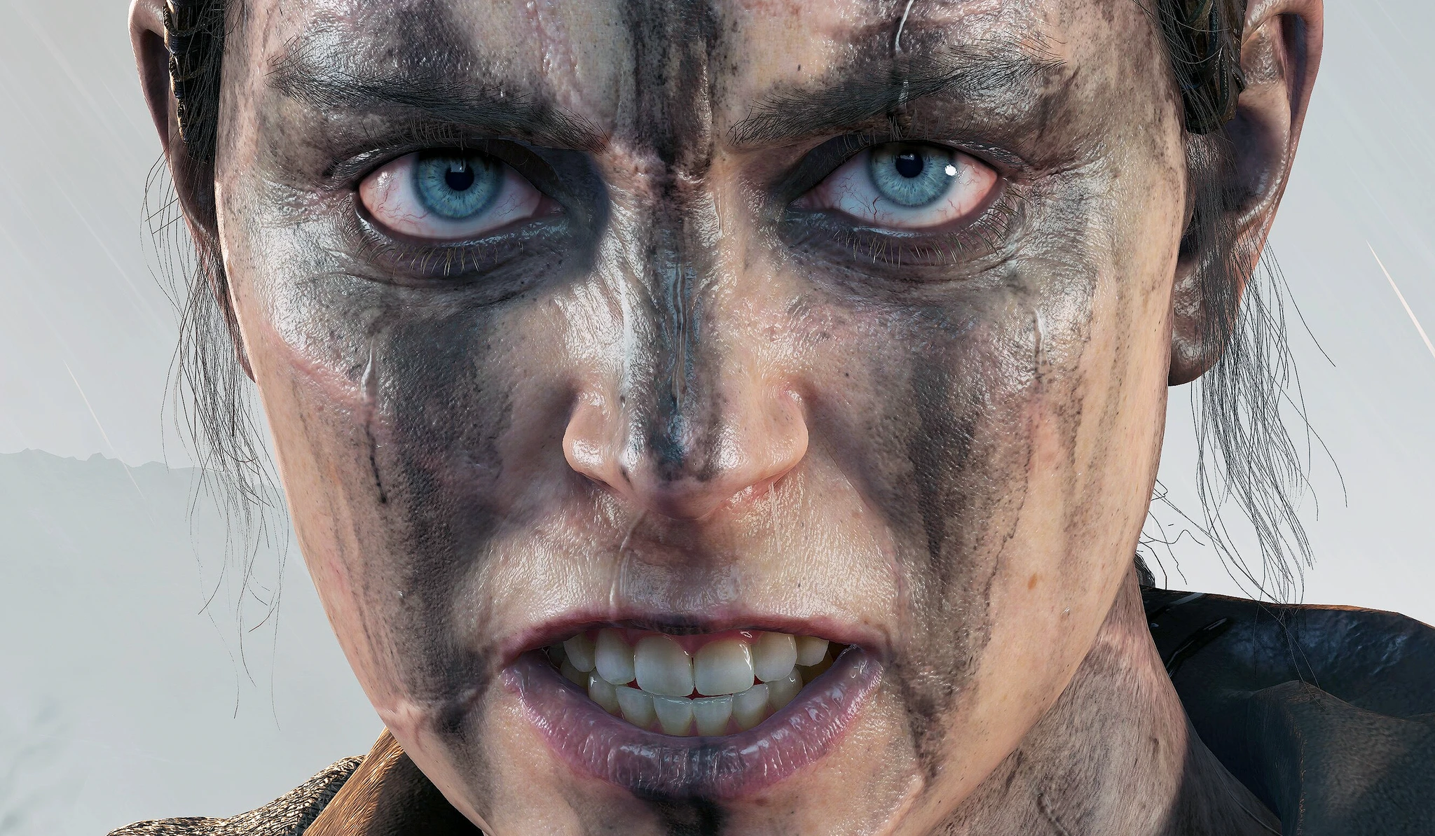 Extrem närbild på Senua i Senua's Saga: Hellblade II, med smutsstreck över ansiktet, ljusblå ögon och sammanbitna tänder i en dimmig miljö.