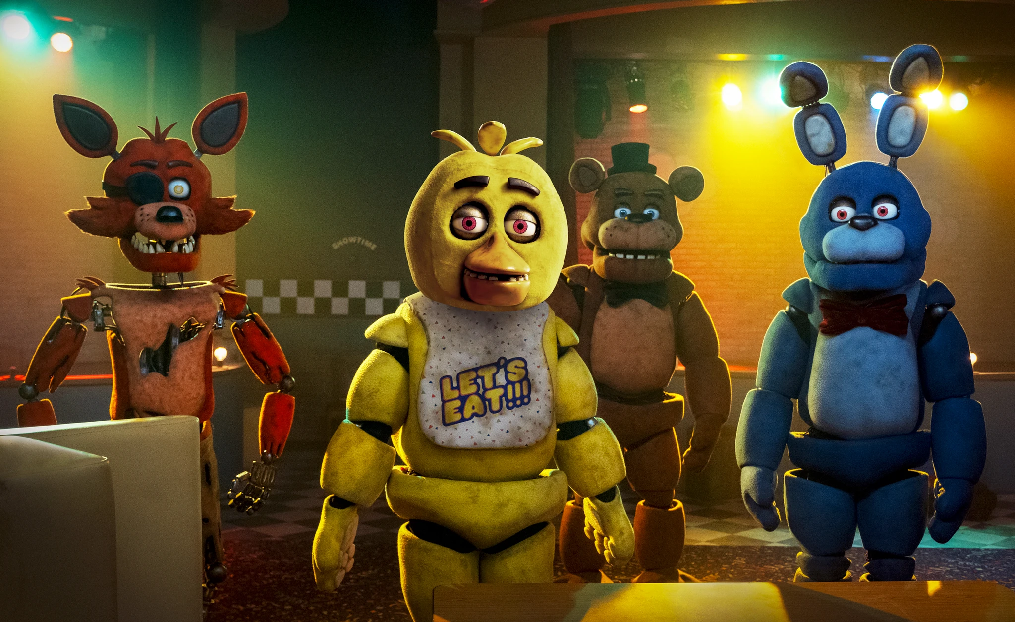 Animatroniska figurerna Foxy, Chica, Freddy och Bonnie står på rad i en dunkel pizzeria med färgade strålkastare. Chica bär haklappen "Let's eat!!!".