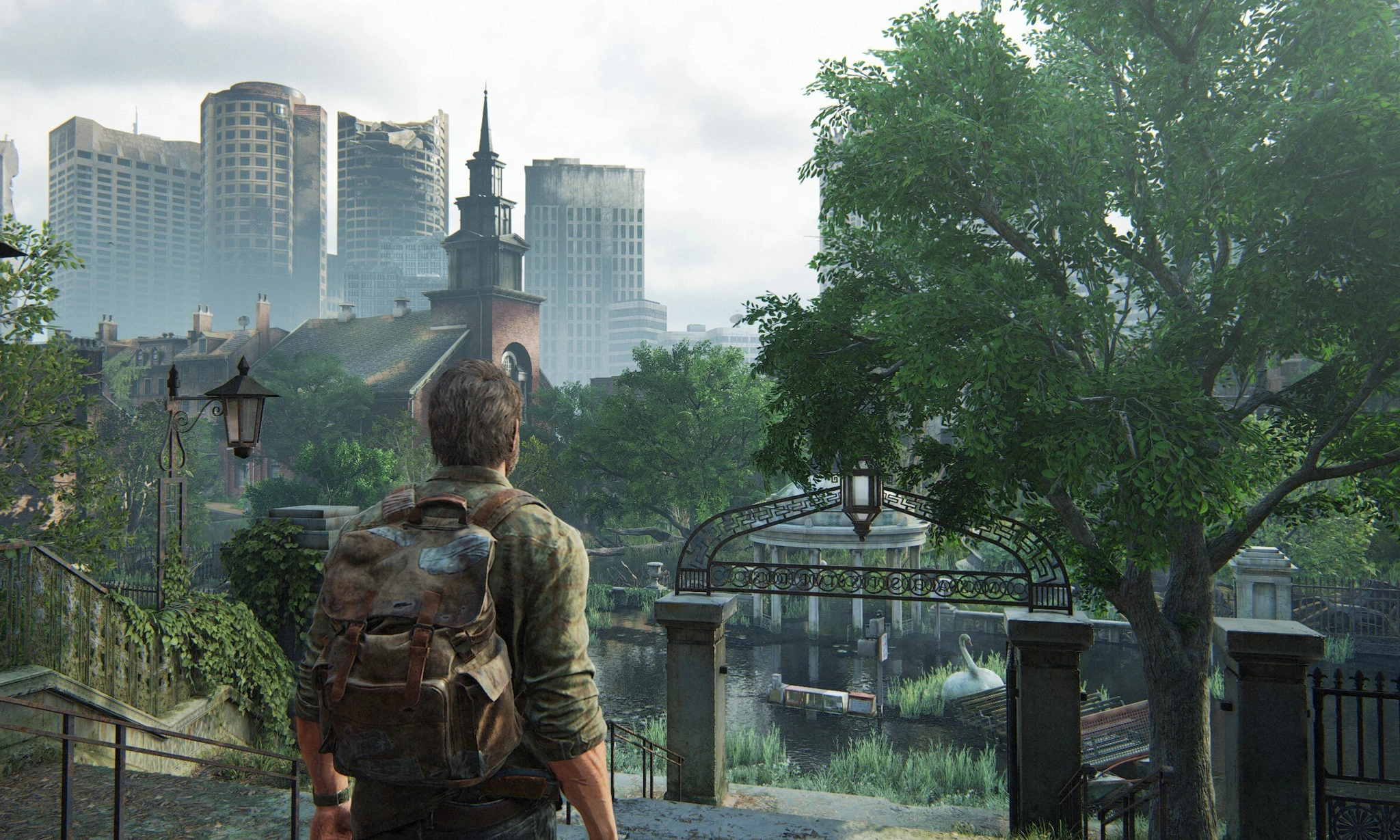Man med ryggsäck sedd bakifrån blickar ut över en övergiven, igenvuxen stad med höghus, en kyrka och en damm i The Last of Us.