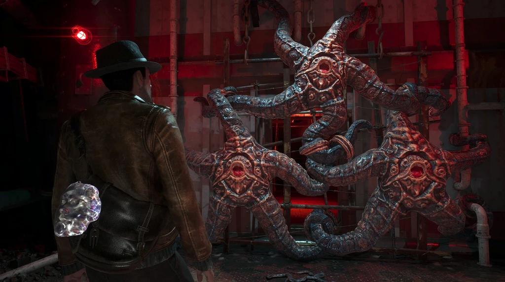 Detektiven i hatt och skinnjacka står framför tre stora tentakelliknande stenfigurer med ögon i ett rödbelyst, rostigt rum i The Sinking City 2.