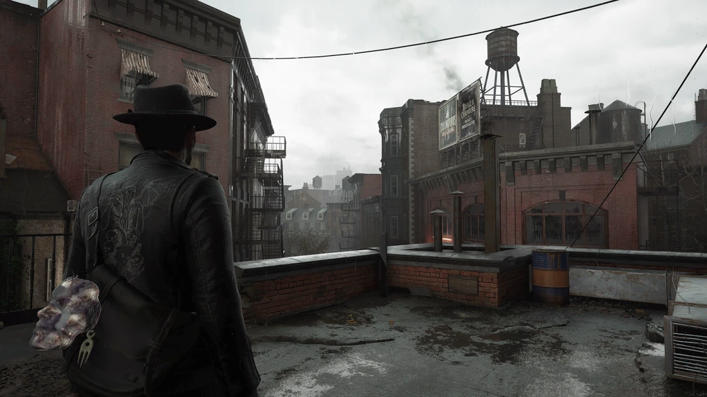 Privatdetektiven i hatt och mörk skinnjacka står med ryggen mot oss på ett regnvått tak i The Sinking City 2 och blickar ut över förfallna tegelhus och ett vattentorn.