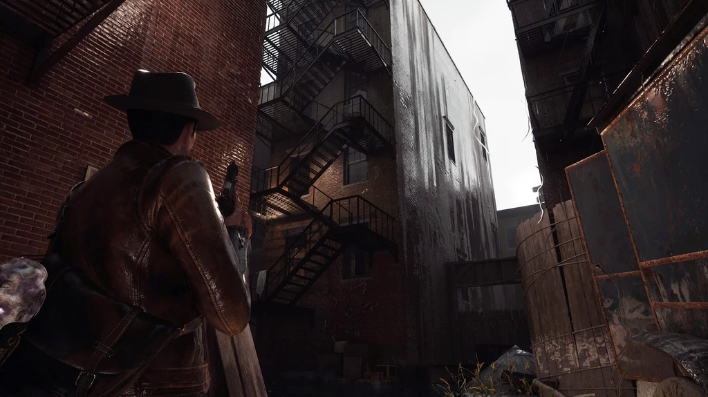 Spelaren i hatt och skinnjacka håller en pistol redo i en smal, skuggig bakgata i The Sinking City 2, mellan rödbruna tegelhus och rostiga brandtrappor.