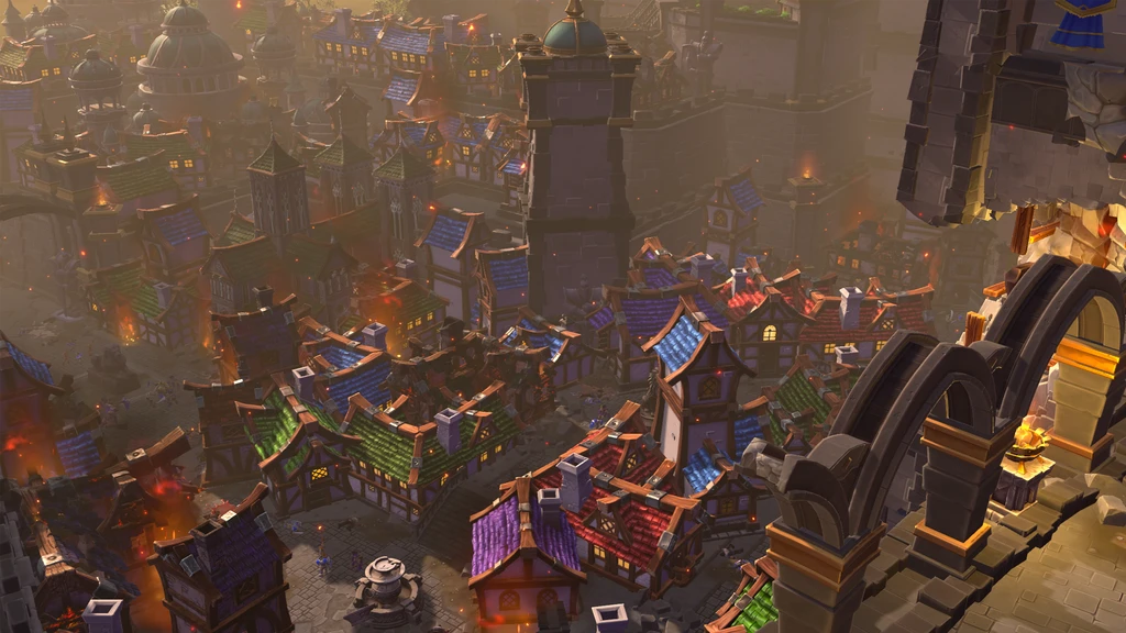 Warcraft III: Reforged. Överblick över en tät medeltidsstad med färgglada tak i blått, grönt och rött, där eld och rök stiger från flera byggnader.