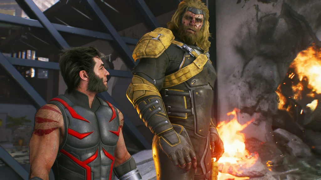 Wolverine i grå och röd dräkt tittar upp mot en lång, blond och skäggig man i gul och svart rustning, medan eldar brinner i det raserade rummet bakom dem.