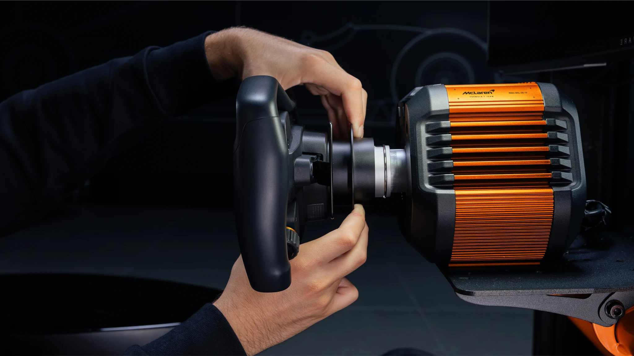 Två händer sätter fast en svart ratt på den orange och grå direktdrivna basen med McLaren-logotyp, en racingratt för simracing.