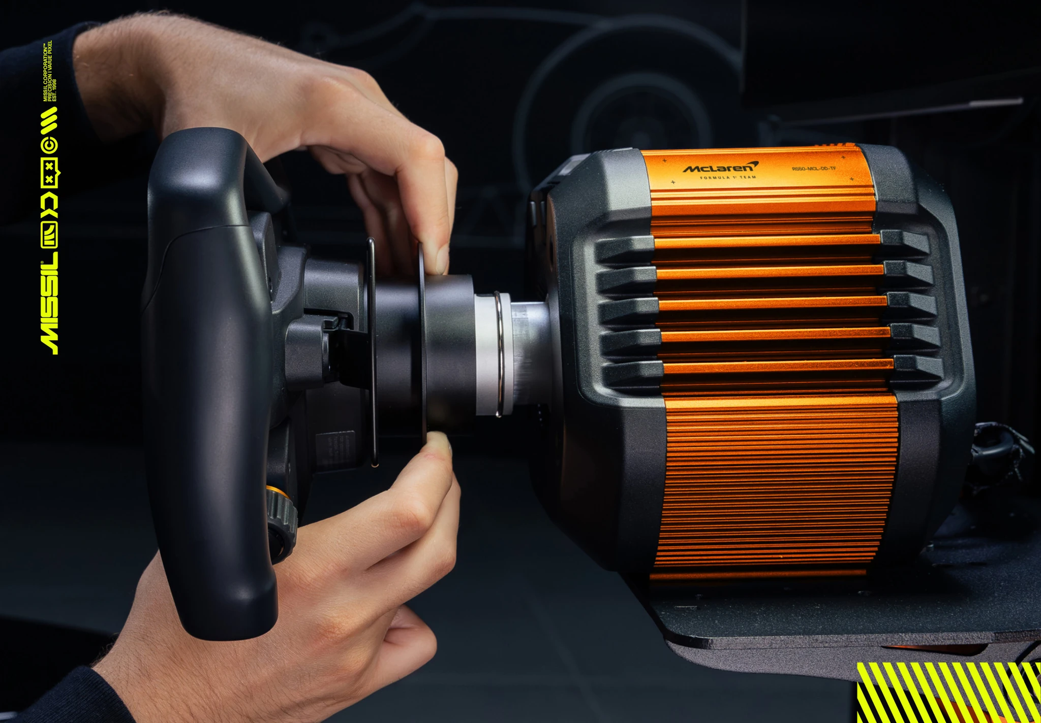 Två händer fäster ett svart ratt på en orange McLaren-märkt direct drive-bas för racingspel, sedda från sidan mot mörk bakgrund.