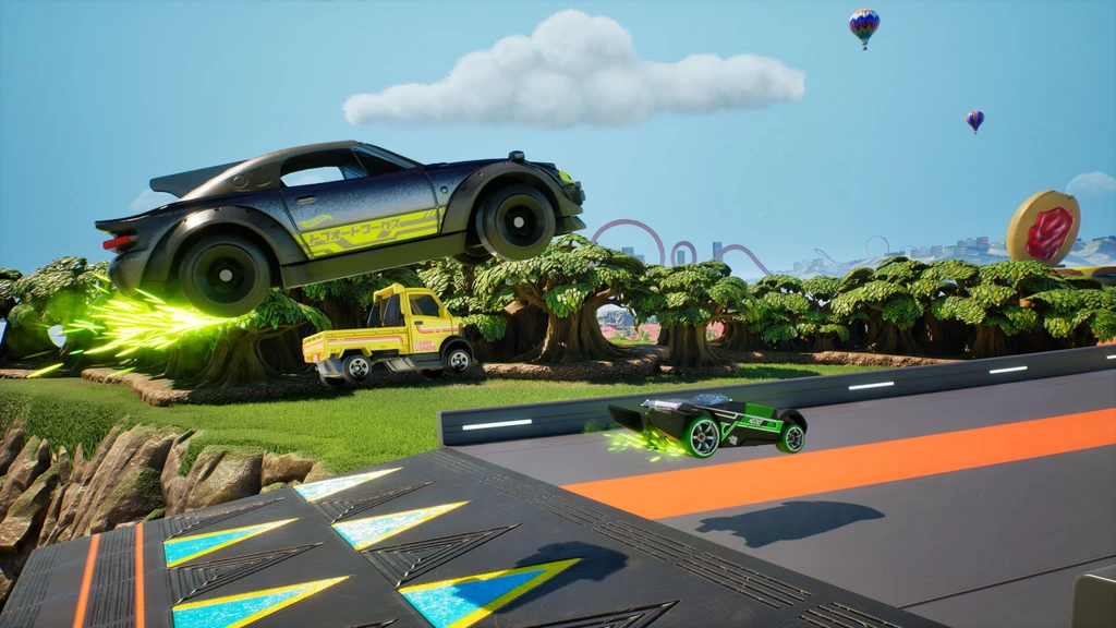 Hot Wheels Infinite Rush: en svart bil med gröna turboflammor flyger över en orange och grå bana, medan en liten grön bil kör på banan och ballonger syns på himlen.