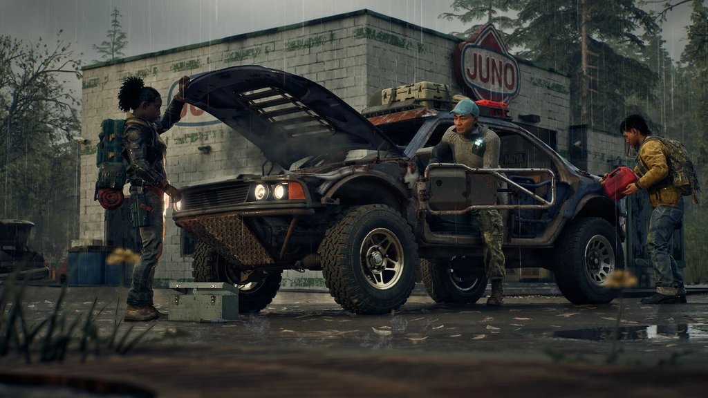 Tre överlevare reparerar en pansrad pickup med uppfälld motorhuv framför en regnvåt bensinstation med skylten Juno, i State of Decay 3.