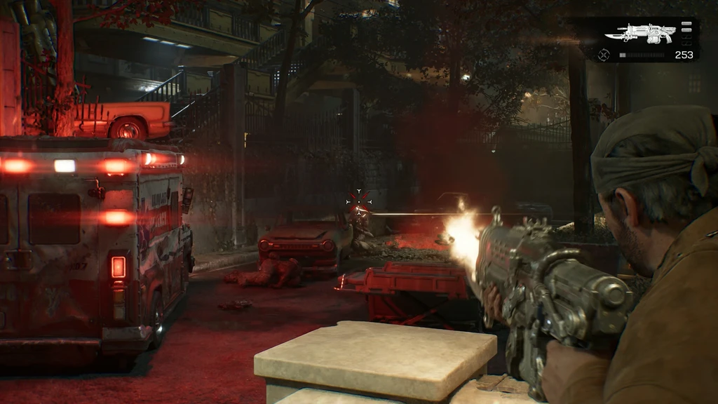 Gears of War: E-Day. En soldat med bandana skjuter med ett Lancer-gevär från skydd bakom en betongmur mot en fiende på en röddränkt gata med ambulans och vrak.