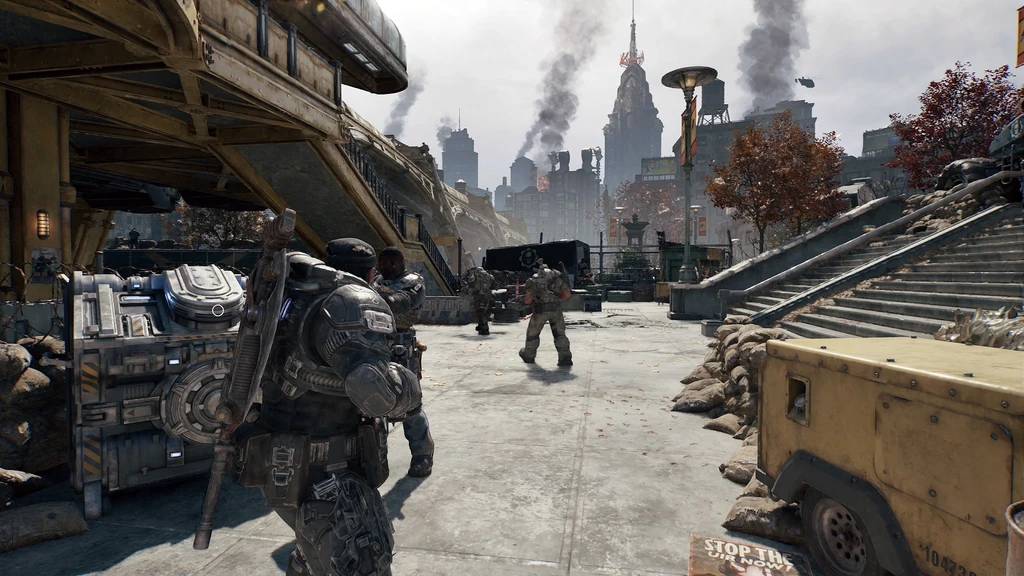 Tungt bepansrade soldater i Gears of War: E-Day rör sig över ett öppet torg i en förstörd stad, med rök som stiger bland skyskraporna och en trappa till höger.