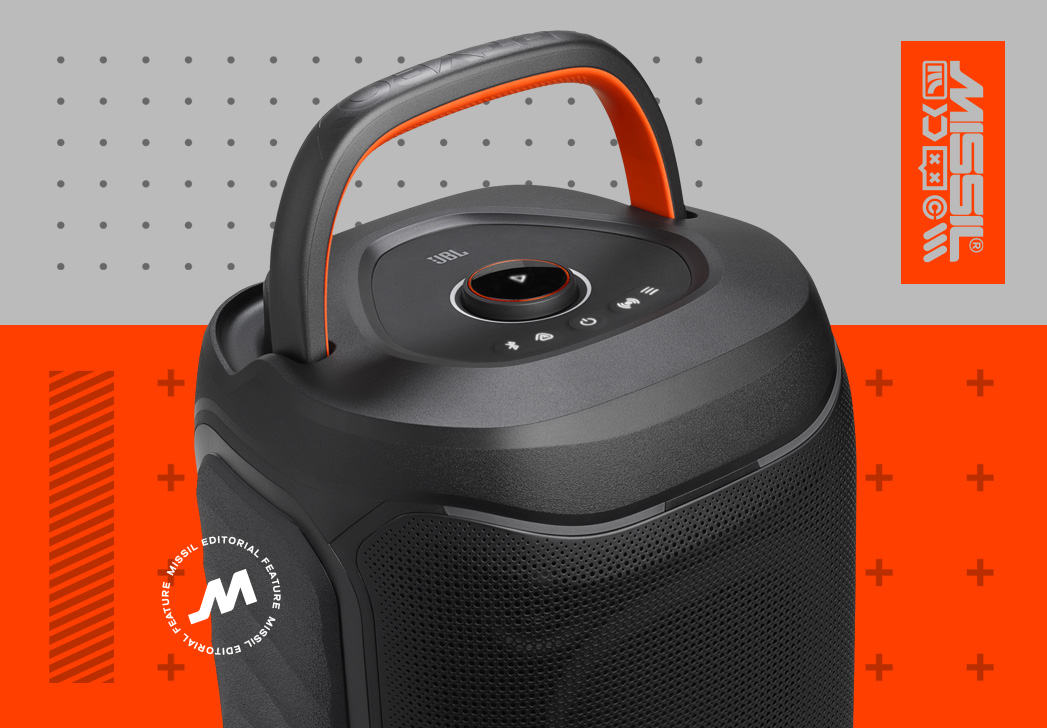 Svart bärbar JBL-högtalare sedd uppifrån med orange bärhandtag och knappar på ovansidan, mot grå och orange bakgrund med MISSIL-logotyp.