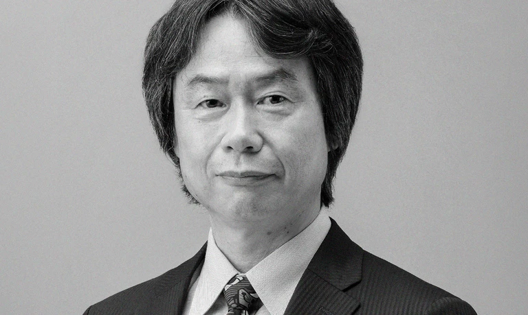 Svartvitt porträtt av Shigeru Miyamoto, en man med mörkt, tidstypiskt page-liknande hår, kostym, skjorta och mönstrad slips, som tittar rakt in i kameran med allvarlig min.