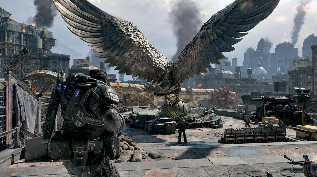 Soldat i tung rustning ses bakifrån på ett stridsskadat tak i Gears of War: E-Day, med en gigantisk metallörn med utsträckta vingar och rökpelare över staden.