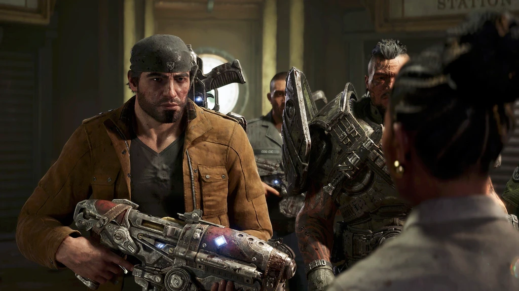 Skäggig man i mössa och brun jacka håller ett tungt, skrymmande vapen medan pansrade soldater samlas bakom honom i en mörk stationslokal i Gears of War: E-Day.