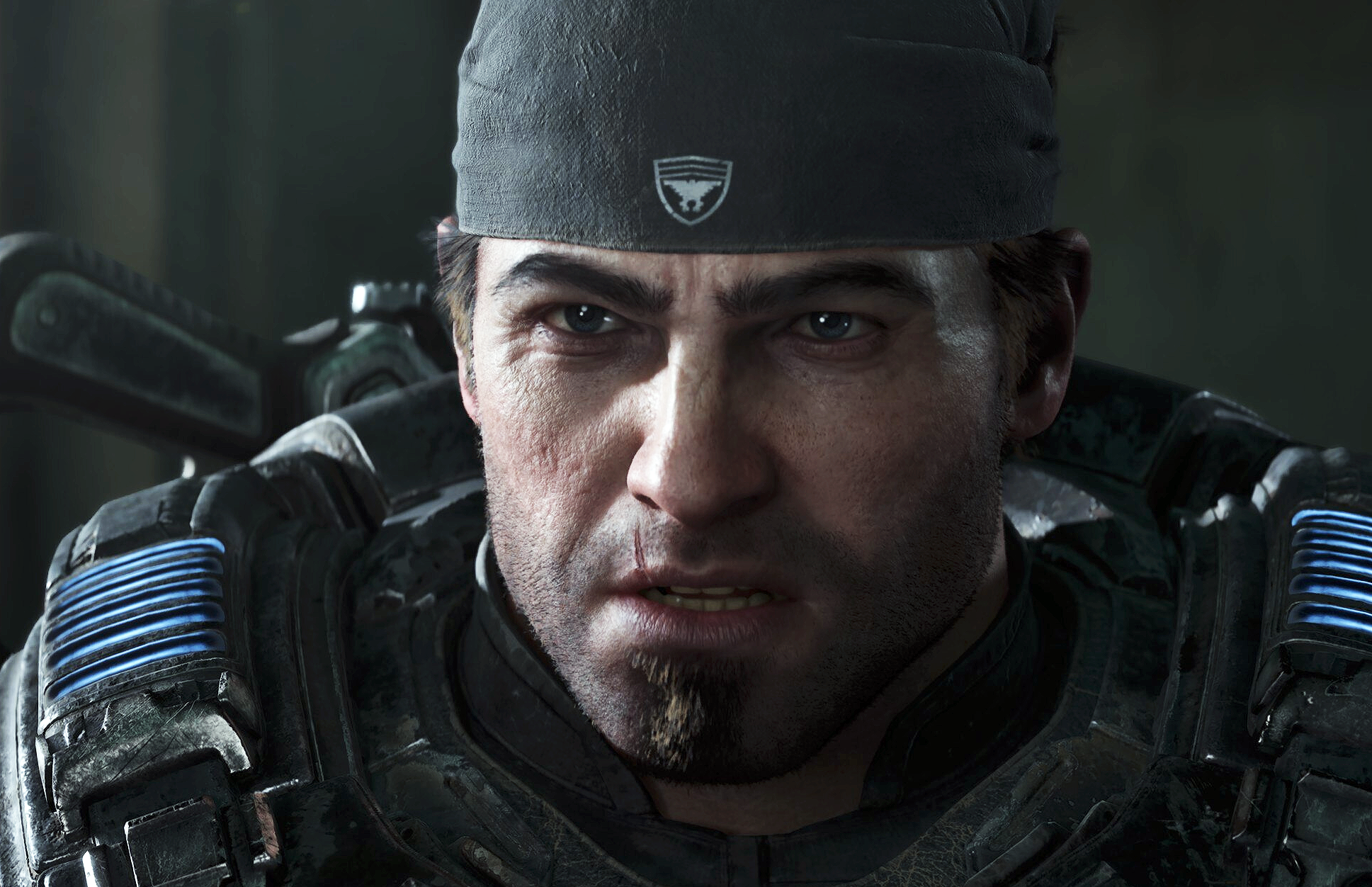 Närbild på en sliten, skäggstubbad man i bandana och tung grå rustning med blå lysande detaljer, ur Gears of War: E-Day.