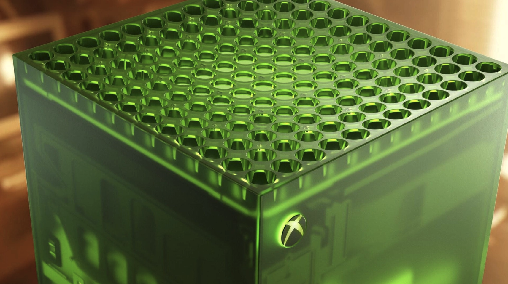 Närbild på en genomskinlig grön Xbox Series X med hålmönstrad ovansida och Xbox-logotypen på sidan, mot suddig brun bakgrund.