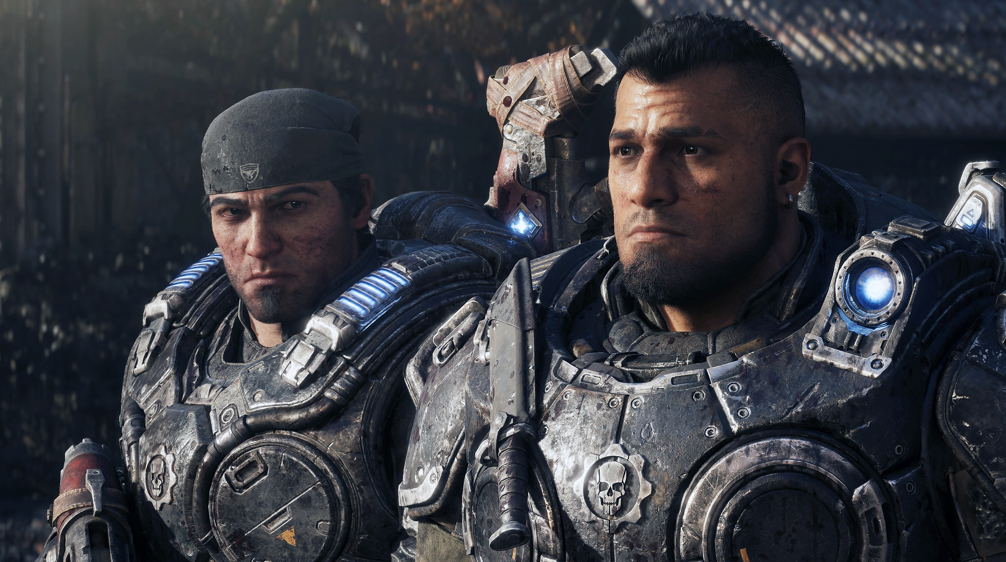 Två allvarsamma soldater i slitna, skrovliga rustningar med blå lampor står sida vid sida i en mörk miljö i Gears of War: E-Day.