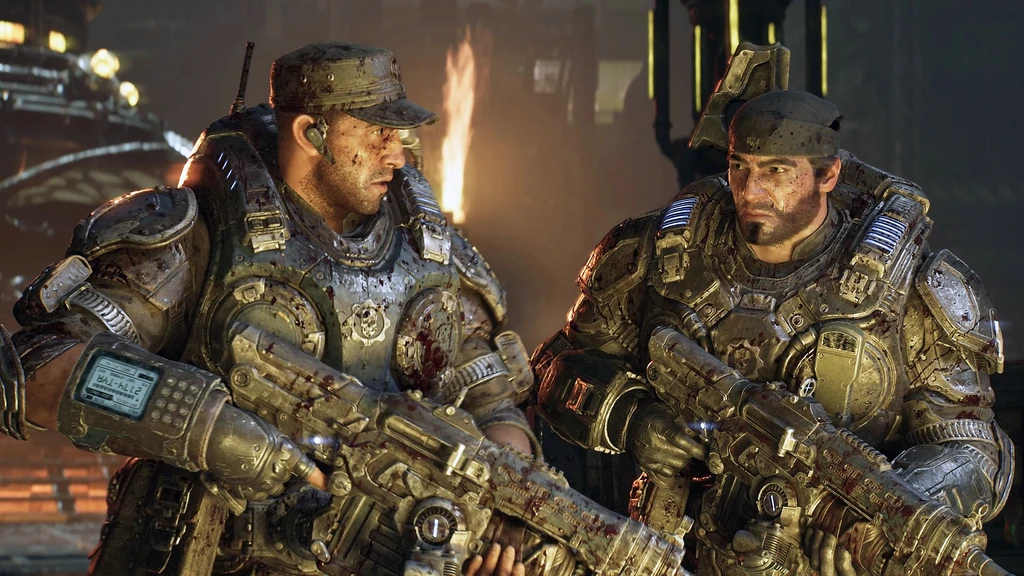 Två smutsiga, blodstänkta soldater i tung rustning står sida vid sida med gevär i händerna i en mörk miljö med eld i bakgrunden, från Gears of War: E-Day.