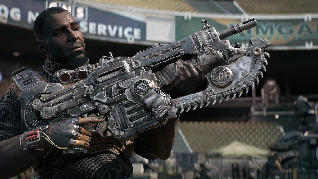 En man med skyddsglasögon runt halsen håller upp ett Lancer-gevär med motorsågsbajonett framför en övergiven arena i Gears of War: E-Day.