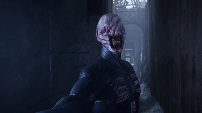 En cenobit i svart läderdräkt med sydd, blodig hud och blottade tänder står i en mörk, smal stenkorridor i Hellraiser: Revival och sträcker ut handen mot kameran.